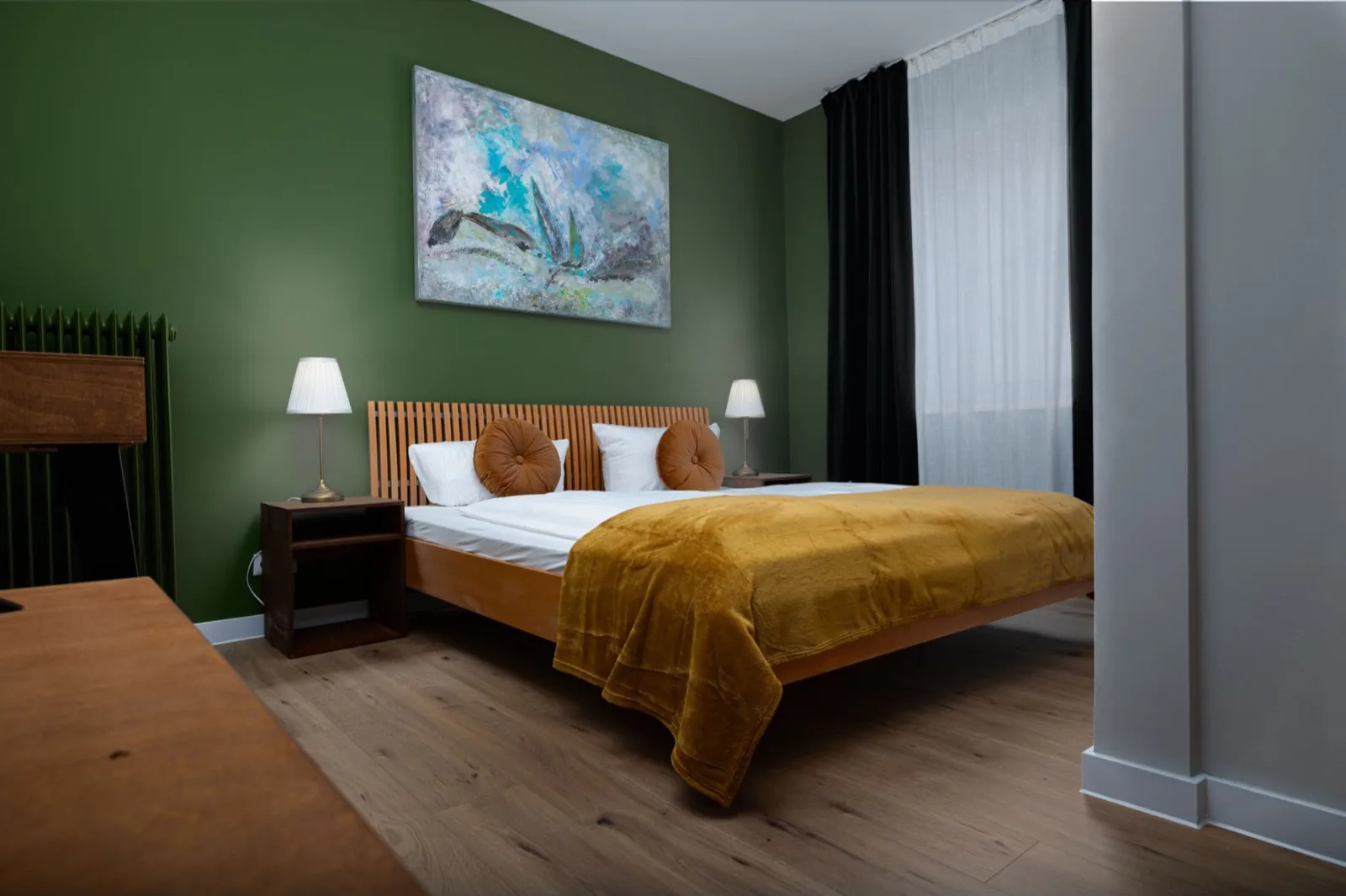 Doppelzimmer mit grünem Bett und Kunst an der Wand